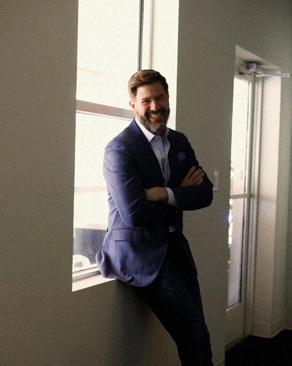 Jeremy Straub, leaning against a window in a navy blazer, smiling