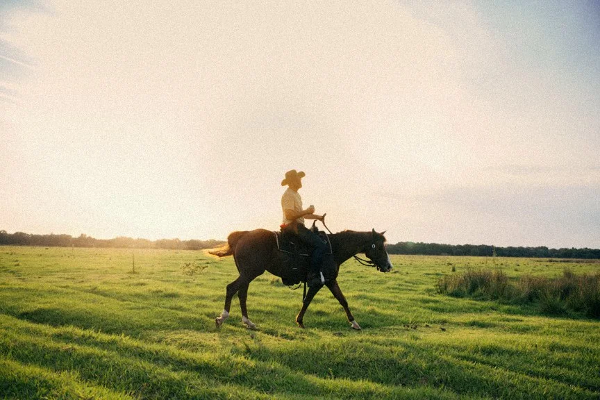 Jeremy on horseback crossing an open field at golden hour